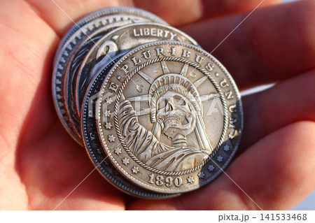 Souvenir coin Morgan dollar with the image of the Statue of Liberty in the form of a skeleton, stack of Hobo Nickel coins in hand 141533468