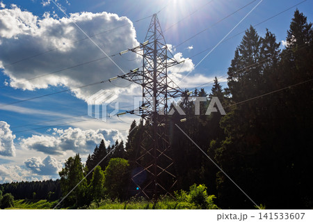 Steel high voltage electricity transmission tower standing against a vivid blue sky with bright sunbeams shining through clouds in a rural forest landscape area Steel high voltage electricity transmission tower standing against a vivid blue sky with bright sunbeams shining through clouds in a rural forest landscape area 141533607