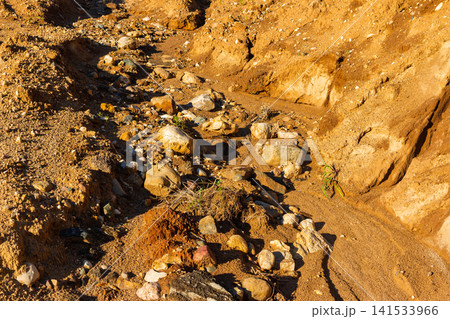 Rugged earth texture of a dried creek bed filled with scattered stones and gravel, showcasing natural erosion patterns under warm golden hour sunlight in a wild outdoor environment Rugged earth texture of a dried creek bed filled with scattered stones and gravel, showcasing natural erosion patterns under warm golden hour sunlight in a wild outdoor environment 141533966