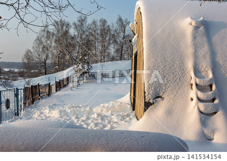 Arch-shaped barn covered in thick snow with a snow-draped ladder on its side, bathed in soft evening light amidst a winter landscape Arch-shaped barn covered in thick snow with a snow-draped ladder on its side, bathed in soft evening light amidst a winter landscape 141534154