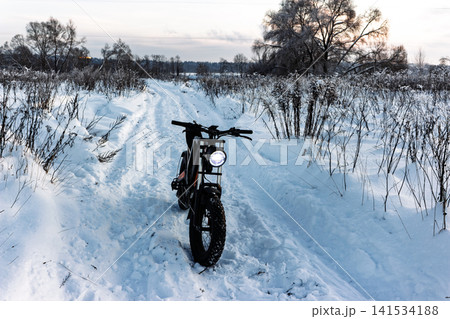 Robust electric fat bike, headlight glowing, navigates fresh powder on a serene winter trail. A cool ride for snowy adventures Robust electric fat bike, headlight glowing, navigates fresh powder on a serene winter trail. A cool ride for snowy adventures 141534188