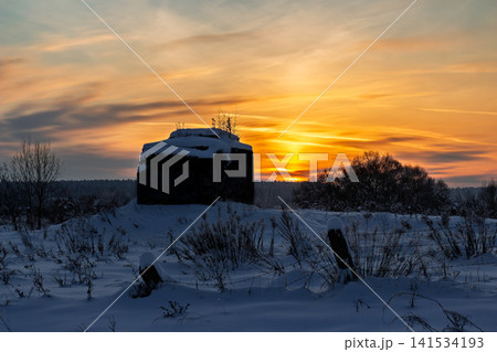 A snow-dusted, forgotten bunker stands silhouetted against a breathtaking winter sunset. Golden hour hues illuminate the frosty landscape, evoking serene solitude A snow-dusted, forgotten bunker stands silhouetted against a breathtaking winter sunset. Golden hour hues illuminate the frosty landscape, evoking serene solitude 141534193