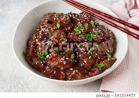 Crispy beef, with green onions and sesame seeds, in a bowl with chopsticks, on a textured surface, on a light background, no people Crispy beef, with green onions and sesame seeds, in a bowl with chopsticks, on a textured surface, on a light background, no people 141534477