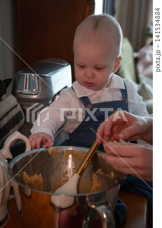 Curious baby tastes homemade almond cookie dough while family prepares dessert together in cozy kitchen at home. Childhood, family baking, parenting, learning, home cooking, lifestyle, togetherness 141534884