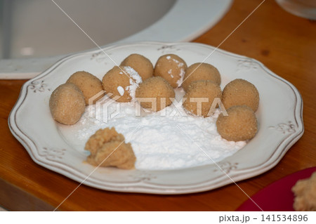 Homemade almond cookie dough balls rest on powdered sugar before baking on decorative plate in family kitchen. Home baking, dessert, recipe, pastry preparation, food styling, cooking, lifestyle Homemade almond cookie dough balls rest on powdered sugar before baking on decorative plate in family kitchen. Home baking, dessert, recipe, pastry preparation, food styling, cooking, lifestyle 141534896