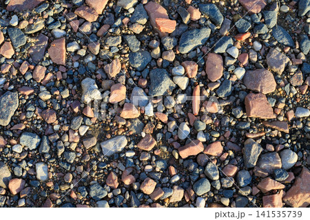 Texture of a rural road with sand, pebbles, and crushed stone. Natural gravel surface and geological background. Mixed granite stones on a coastal strip Texture of a rural road with sand, pebbles, and crushed stone. Natural gravel surface and geological background. Mixed granite stones on a coastal strip 141535739