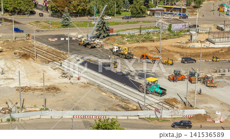 Asphalt paver, roller and truck on the road repair site during asphalting timelapse. Road construction equipment. Asphalt paver, roller and truck on the road repair site during asphalting timelapse. Road construction equipment. 141536589