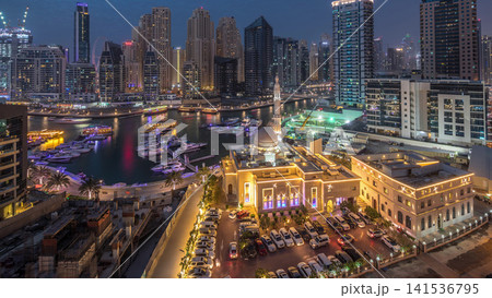 Yachts in Dubai Marina flanked by the Al Rahim Mosque and residential towers and skyscrapers aerial day to night timelapse. 141536795