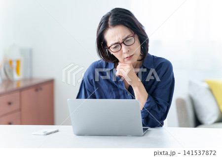 老眼鏡をかけてパソコンを使う中高年女性 老眼鏡をかけてパソコンを使う中高年女性 141537872