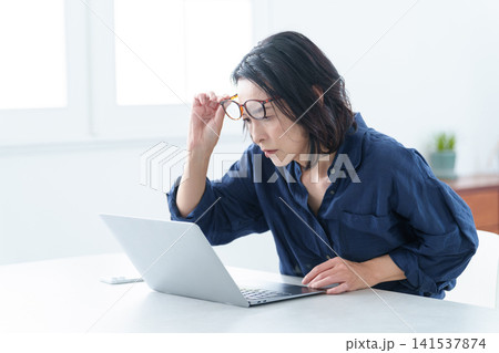 老眼鏡をかけてパソコンを使う中高年女性 老眼鏡をかけてパソコンを使う中高年女性 141537874