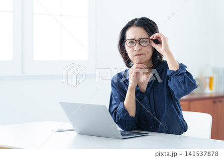 老眼鏡をかけてパソコンを使う中高年女性 老眼鏡をかけてパソコンを使う中高年女性 141537878