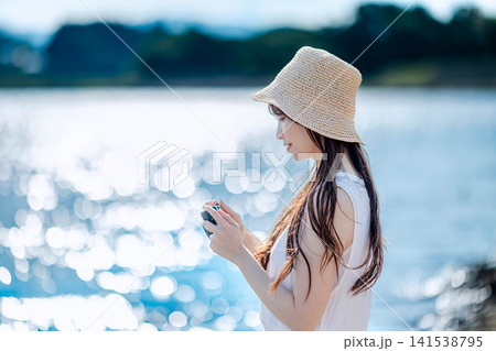 湖畔でフィルムカメラを構える麦わら帽子の女性 湖畔でフィルムカメラを構える麦わら帽子の女性 141538795