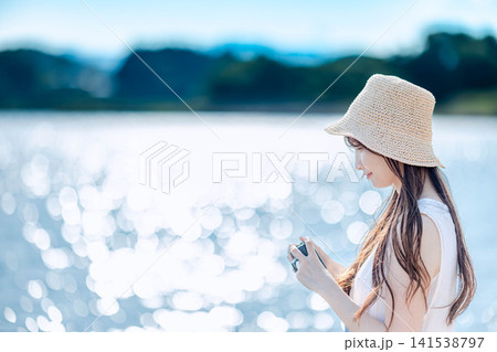 湖畔で光を背にカメラを構える白ワンピースの女性 141538797