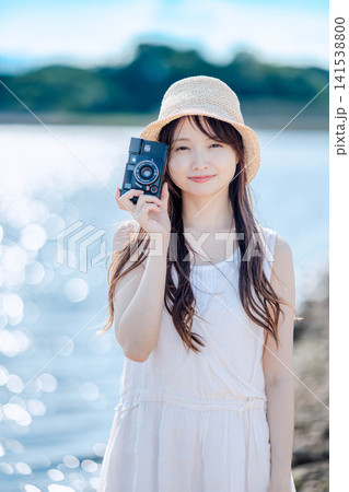 湖を背景にフィルムカメラを構える白ワンピースの女性 湖を背景にフィルムカメラを構える白ワンピースの女性 141538800