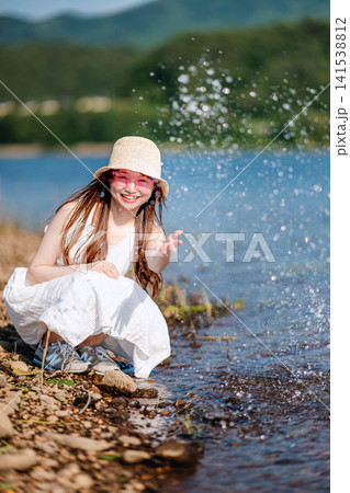 湖畔で水しぶきを上げてはしゃぐ麦わら帽子の女性 湖畔で水しぶきを上げてはしゃぐ麦わら帽子の女性 141538812
