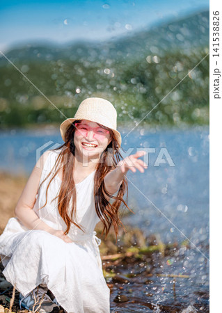 湖畔で水しぶきを上げて笑う麦わら帽子の女性 湖畔で水しぶきを上げて笑う麦わら帽子の女性 141538826