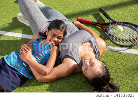 Asian sisters lying side by side wearing sportswear on tennis court near rackets and tennis ball 141539023