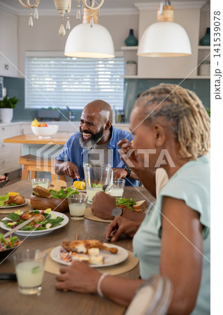African American family sharing grilled chicken meal at wooden dining table in kitchen with pitcher African American family sharing grilled chicken meal at wooden dining table in kitchen with pitcher 141539078
