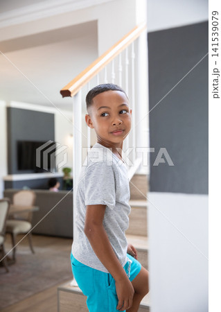 African American school-age boy climbing staircase at home by banister and glancing left at TV African American school-age boy climbing staircase at home by banister and glancing left at TV 141539079