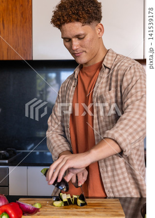 Man slicing eggplant on wooden cutting board at kitchen countertop with chef's knife 141539178