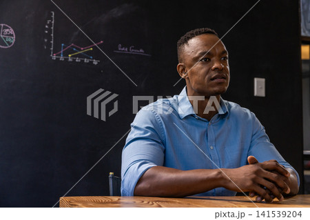 African american man wearing studying chalk diagrams at wooden table, copy space African american man wearing studying chalk diagrams at wooden table, copy space 141539204