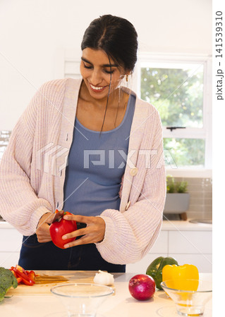 Asian woman slicing red bell pepper on cutting board with broccoli and onion in modern kitchen 141539310