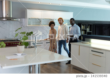 Diverse group touring kitchen with agent in business attire with tablet at island with paperwork 141539340