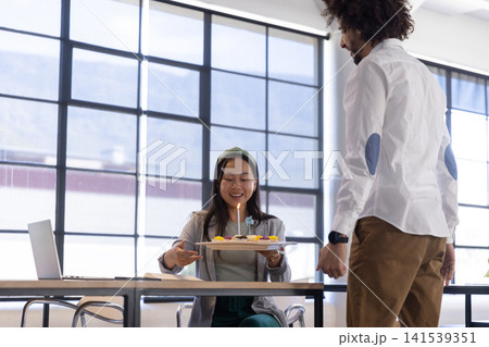 Diverse coworkers celebrating birthday at desk in office holding lit cupcakes, candle by laptop 141539351