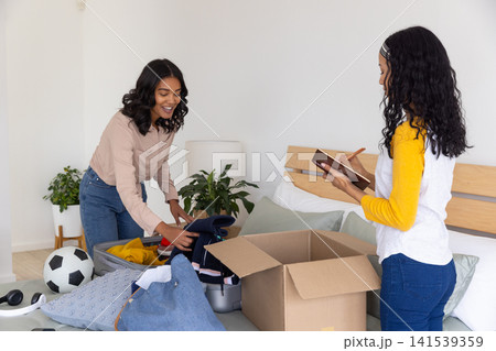 Diverse mom and teenage daughter sorting clothes at home, leaning over suitcase Diverse mom and teenage daughter sorting clothes at home, leaning over suitcase 141539359