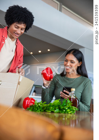 Diverse couple unpacking groceries at modern kitchen table with red bell peppers, smartphone 141539399