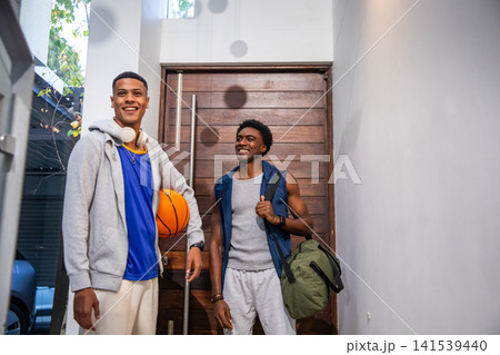 Diverse male friends standing in entryway by wooden door holding basketball and carrying duffle bag Diverse male friends standing in entryway by wooden door holding basketball and carrying duffle bag 141539440