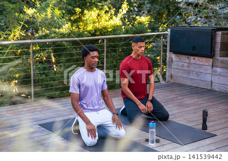 Diverse male friends in sportswear practicing yoga kneeling on deck with mats and water bottles Diverse male friends in sportswear practicing yoga kneeling on deck with mats and water bottles 141539442