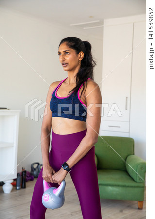 Indian woman performing kettlebell exercise at home holding grey pink kettlebell Indian woman performing kettlebell exercise at home holding grey pink kettlebell 141539852