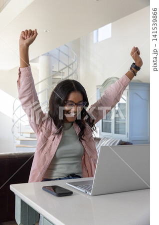 African american woman in 20s celebrating at home desk with laptop smartphone bracelets African american woman in 20s celebrating at home desk with laptop smartphone bracelets 141539866