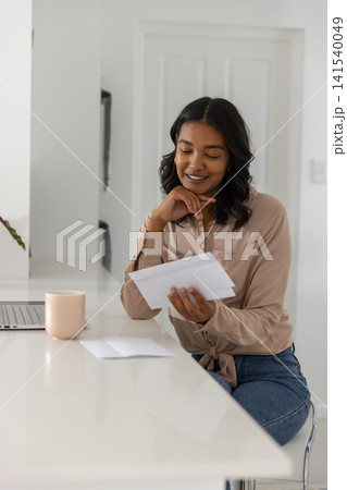 Woman reading letter while sitting at white kitchen countertop Woman reading letter while sitting at white kitchen countertop 141540049