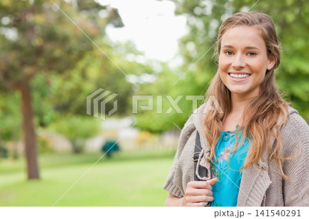 Female standing in park holding bag strap, wearing blue embroidered top, gray cardigan, copy space 141540291