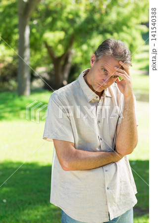 Middle-aged man standing on grassy park lawn wearing light beige button-up shirt and blue jeans Middle-aged man standing on grassy park lawn wearing light beige button-up shirt and blue jeans 141540388