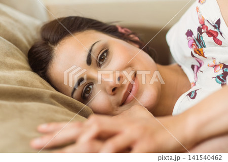 Adult female reclining on beige cushion on sofa at home, wearing white floral top, resting forearm 141540462