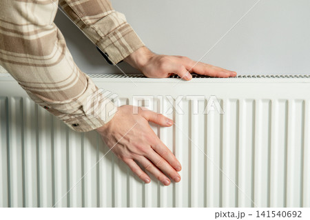 Heating season. Hands press against radiator to feel warmth during heating season 141540692