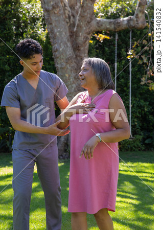 Caregiver wearing scrubs supporting senior woman standing on lawn under tree with rope swing Caregiver wearing scrubs supporting senior woman standing on lawn under tree with rope swing 141540832