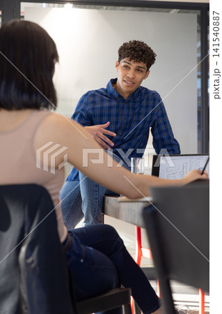 Diverse coworkers discussing laptop sketches at conference table in modern office with water glass 141540887