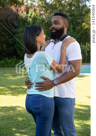 Asian and African American couple holding each other in backyard garden with visible wristwatch 141540904