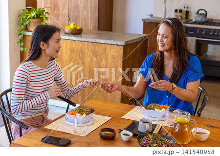 Asian mother and daughter exchanging chopsticks over salad bowls at dining table with iced tea Asian mother and daughter exchanging chopsticks over salad bowls at dining table with iced tea 141540958