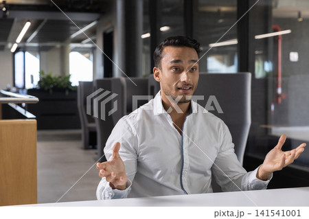 Indian man gesturing while speaking at white table in office with glass partitions Indian man gesturing while speaking at white table in office with glass partitions 141541001