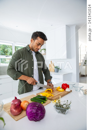 Man slicing bell pepper on cutting board at kitchen island with chef's knife 141541014