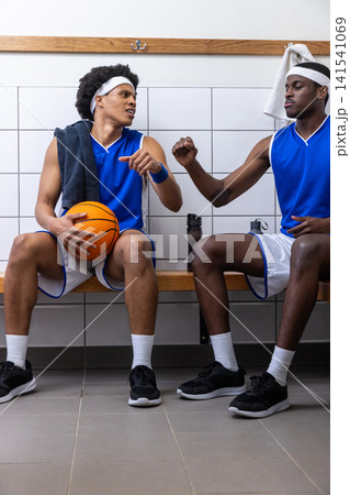 African american male players sitting in locker room with basketball, exchanging fist bump African american male players sitting in locker room with basketball, exchanging fist bump 141541069