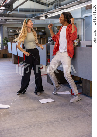 Diverse coworkers dancing near cubicle partitions and desks in open office with scattered paper 141541220