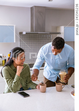 Diverse couple scooping sugar into ribbed ceramic mugs on white quartz countertop in kitchen Diverse couple scooping sugar into ribbed ceramic mugs on white quartz countertop in kitchen 141541236