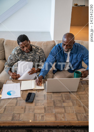 African american father and son reviewing charts with him in camouflage uniform on couch 141541290