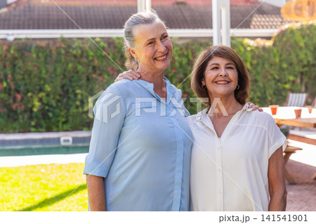 Senior friends standing in backyard by pool and hedge beside picnic table with orange cups Senior friends standing in backyard by pool and hedge beside picnic table with orange cups 141541901